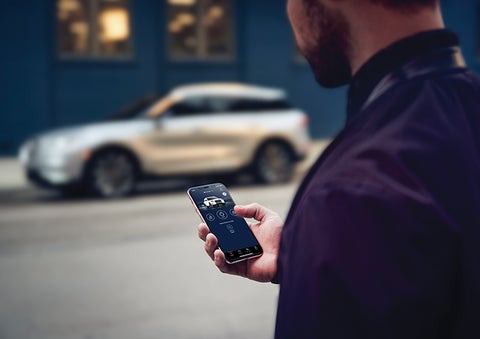 A person is shown interacting with a smartphone to connect to a Lincoln vehicle across the street. | Gray-Daniels Lincoln in Brandon MS