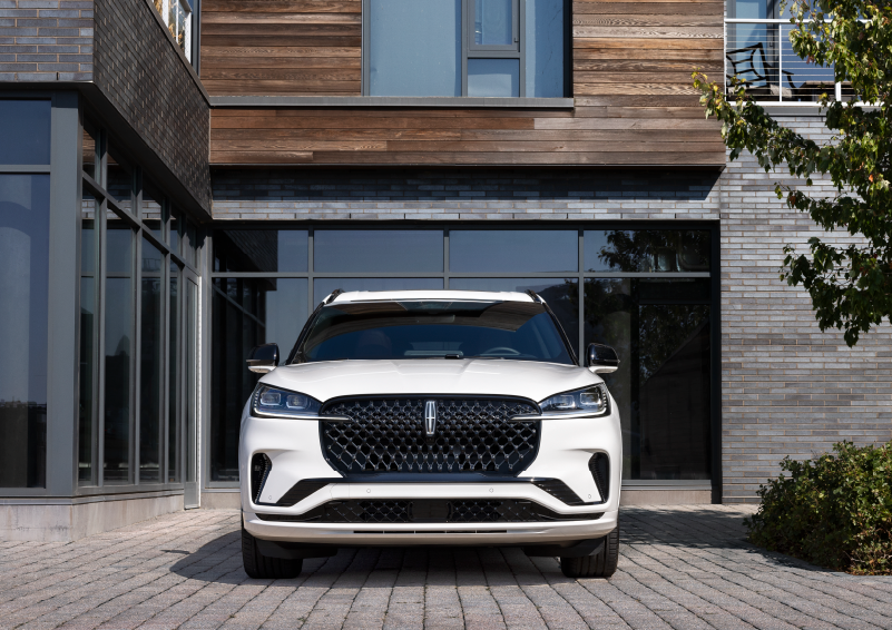 A white 2025 Lincoln Aviator® SUV is shown parked outside a modern building with gray brick and wood accents. | Gray-Daniels Lincoln in Brandon MS