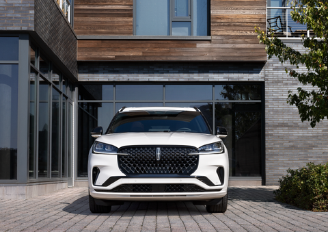 A white 2025 Lincoln Aviator® SUV is shown parked outside a modern building with gray brick and wood accents. | Gray-Daniels Lincoln in Brandon MS