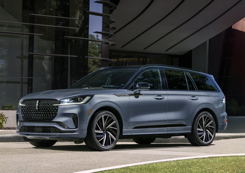 A gray 2025 Lincoln Aviator® SUV is parked outside a modern building showcasing the driver’s side of the vehicle. | Gray-Daniels Lincoln in Brandon MS