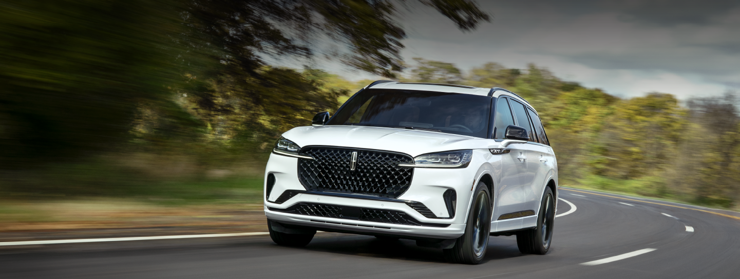 A white 2025 Lincoln Aviator® SUV is being driven down a road lined with trees. | Gray-Daniels Lincoln in Brandon MS