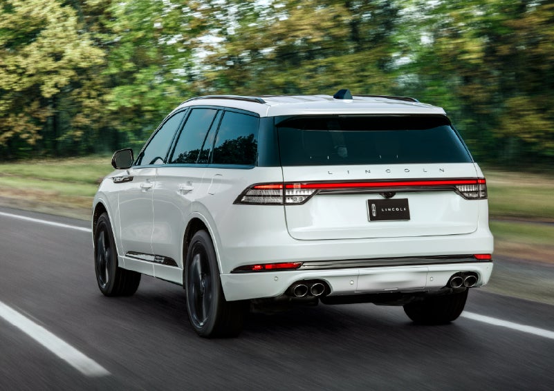 A white 2026 Lincoln Aviator® SUV is being driven away down a road lined with colorful trees. | Gray-Daniels Lincoln in Brandon MS