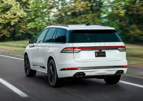 A white 2026 Lincoln Aviator® SUV is being driven away down a road lined with colorful trees. | Gray-Daniels Lincoln in Brandon MS