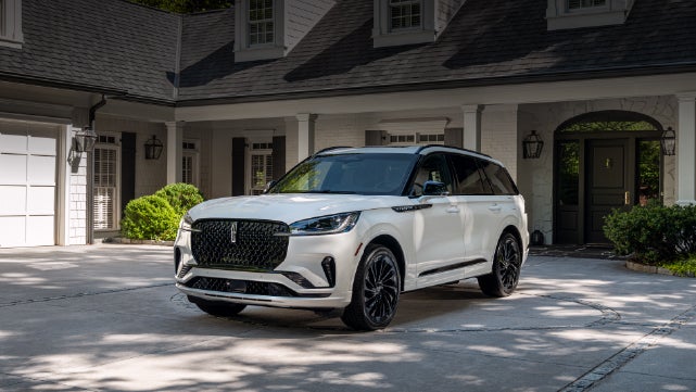 A white 2026 Lincoln Aviator® SUV is parked in the driveway of a luxury home. | Gray-Daniels Lincoln in Brandon MS