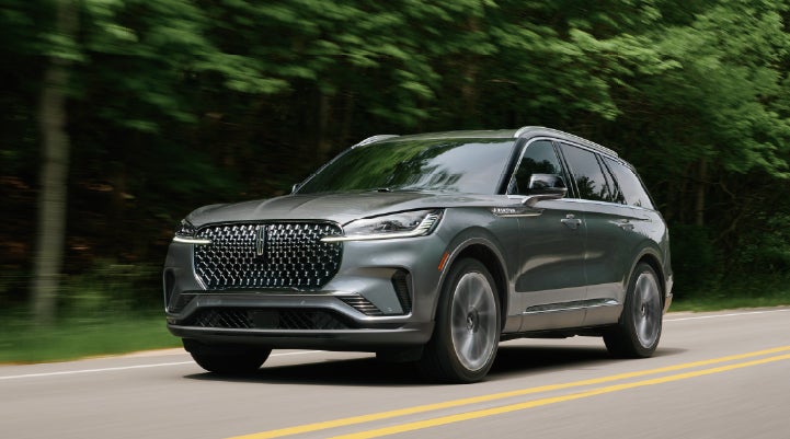 A 2027 Lincoln Aviator® SUV is being driven down a road lined with trees. | Gray-Daniels Lincoln in Brandon MS